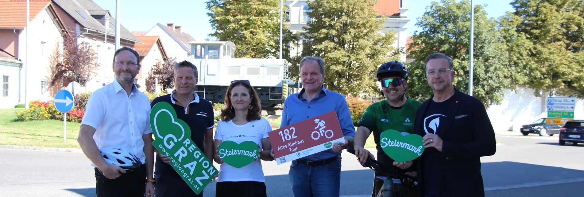 Gruppe mit Rad und Schildern vor dem Bahnhof Köflach