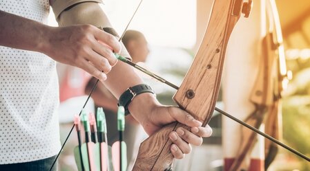 Tourists try to use a bow and arrow and shoot at a target in the amusement park. | © Schilcherland Steiermark | AdobeStock_266956114