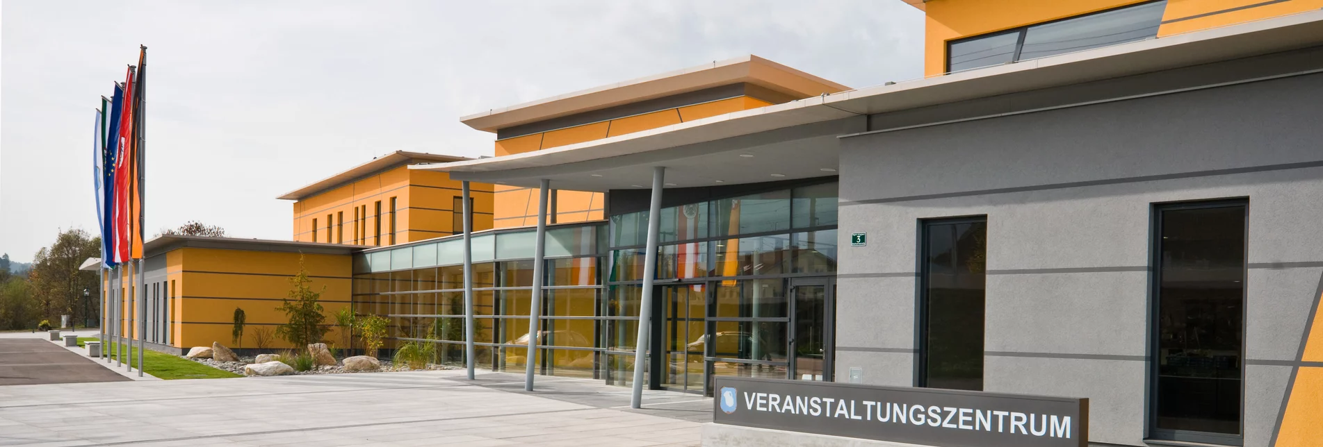 Außenansicht des Veranstaltungszentrums Krieglach mit grau-oranger Fassade und Glaselementen im Eingangsbereich