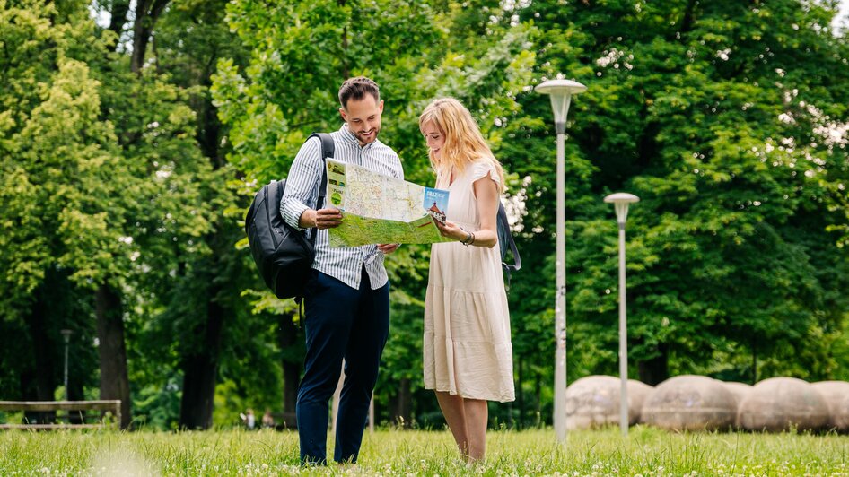 Augarten in Graz I Parks & Gärten in Graz | © Graz Tourismus - Mias Photoart Paar steht im Augarten, schaut auf eine Landkarte. | © Graz Tourismus - Mias Photoart