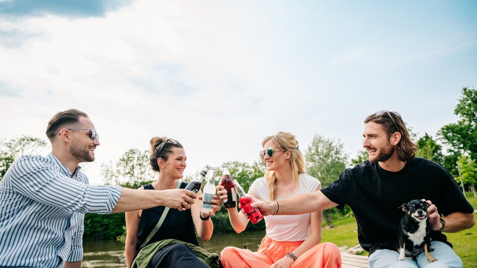 Entspannen im Augarten in Graz I Parks & Gärten in Graz | © Graz Tourismus - Mias Photoart Vier Freunde stoßen mit Getränken am Fluß an. | © Graz Tourismus - Mias Photoart