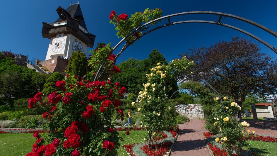 Der Uhrturm auf dem Schlossberg in Graz, umgeben von einem blühenden Garten.