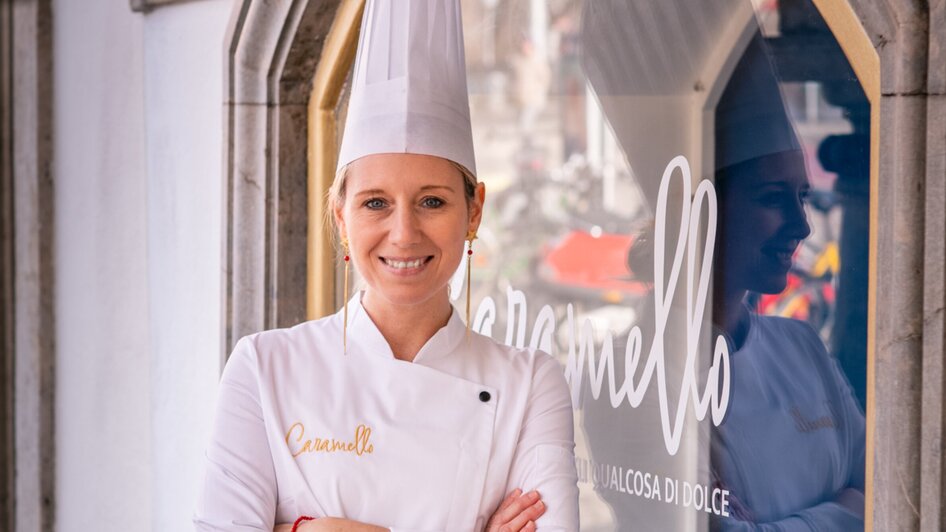 Köchin vor Caffè Caramello in Graz, sie trägt eine Kochjacke und eine Kochmütze.