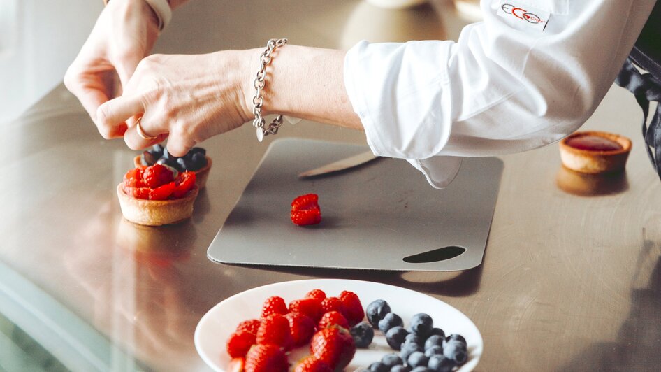 Eine Köchin dekoriert einen Kuchen mit frischen Beeren.