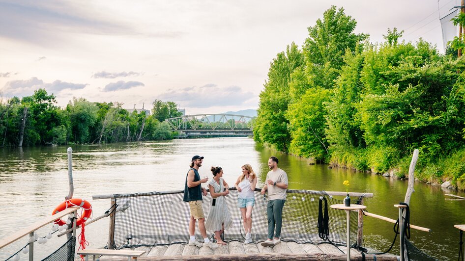 Gruppe von Freunden genießt Zeit am Fluss in Graz, umgeben von Bäumen. | © Graz Tourismus - Mias Photoart