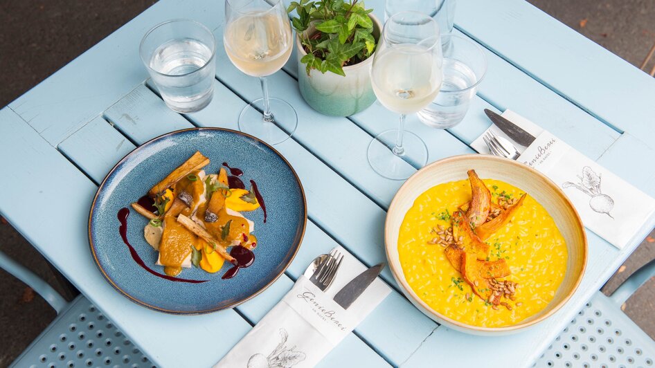 Zwei kunstvoll angerichtete Gerichte auf einem blauen Tisch. | © 5komma5sinne - Helmut Schweighofer