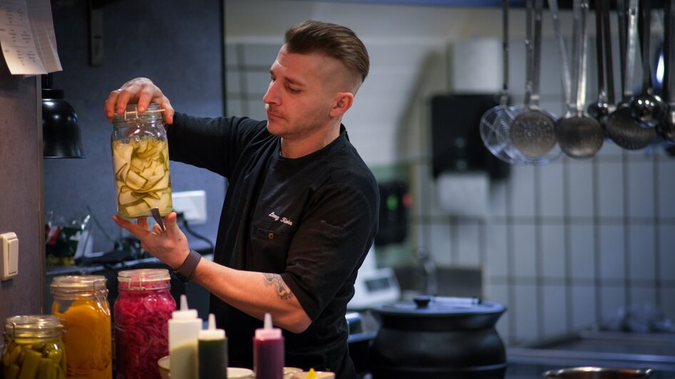 Ein Koch bereitet eingelegtes Gemüse in einer modernen Küche vor.