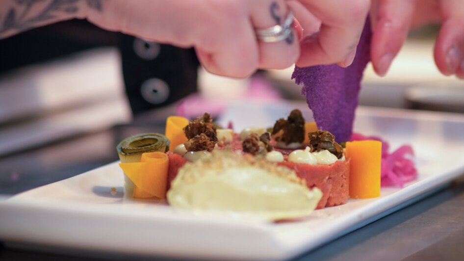 Eine Köchin dekoriert ein Gericht mit bunten Zutaten auf einem Teller.