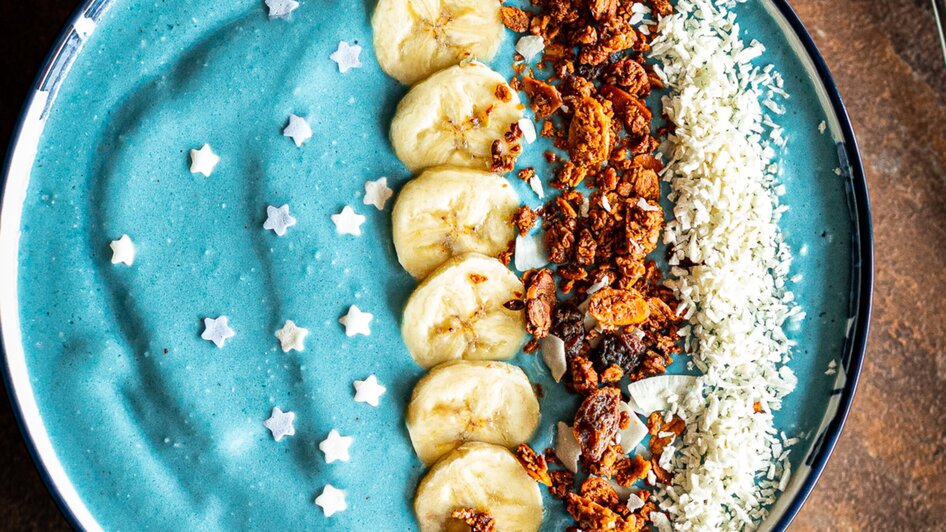 Bunte Smoothiebowl mit Bananen, Granola und Kokosraspeln.