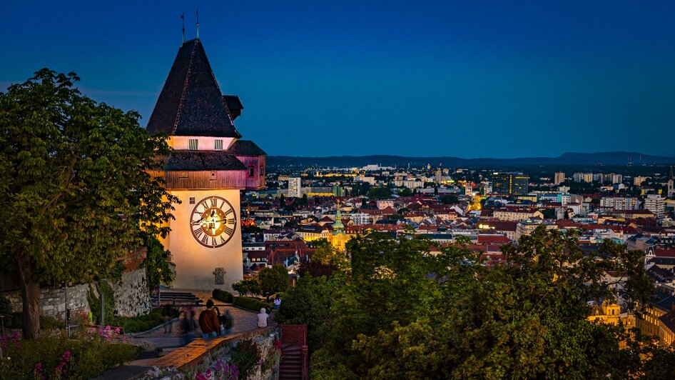 Grazer Uhrturm mit Blick auf die Stadt Graz bei Nacht.
