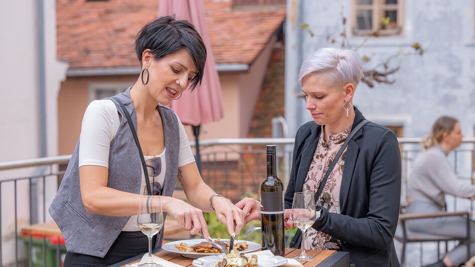 Zwei Frauen genießen das Essen und Wein im Freien bei Gut Schlossberg in Graz.