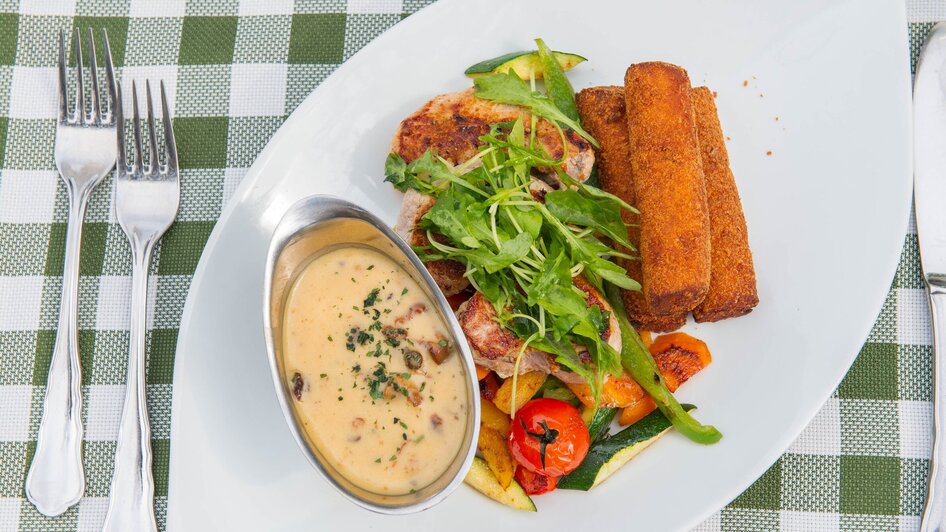 Ein Teller mit gegrilltem Fleisch, Gemüse und Sauce.