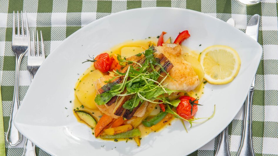 Gegrillter Fisch auf einem Teller mit Gemüse und Kirschtomaten.