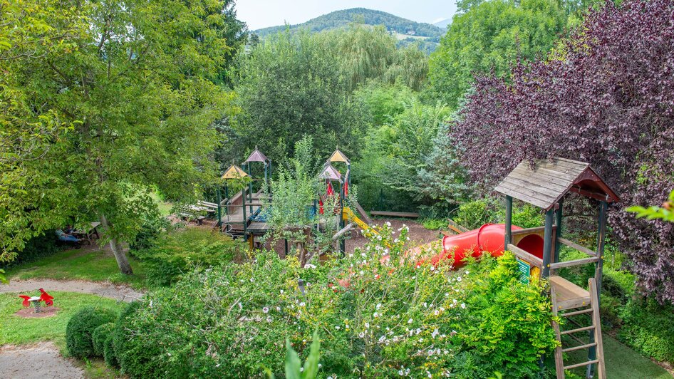 Spielplatz mit Rutschen und Spielgeräten, umgeben von Bäumen.