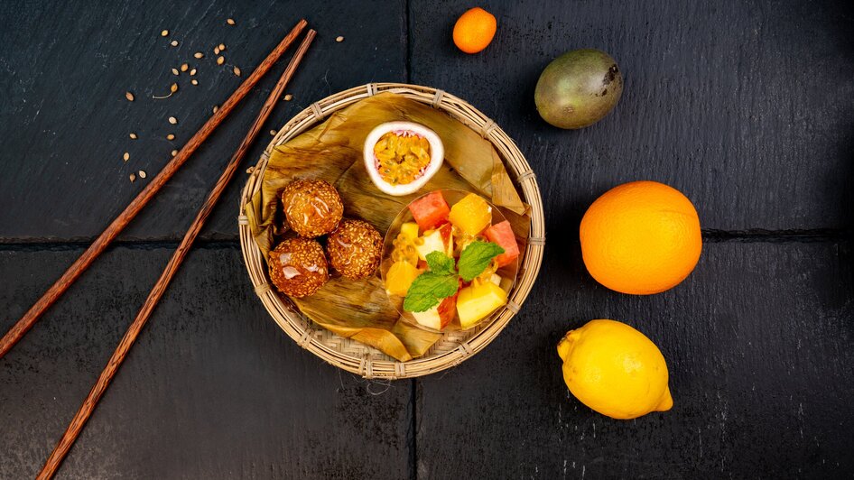 Ein Korb mit verschiedenen Früchten und Snacks, darunter süße Leckereien.