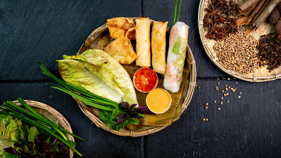 Ein Korb mit verschiedenen vietnamesischen Speisen wie Frühlingsrollen und Dips.