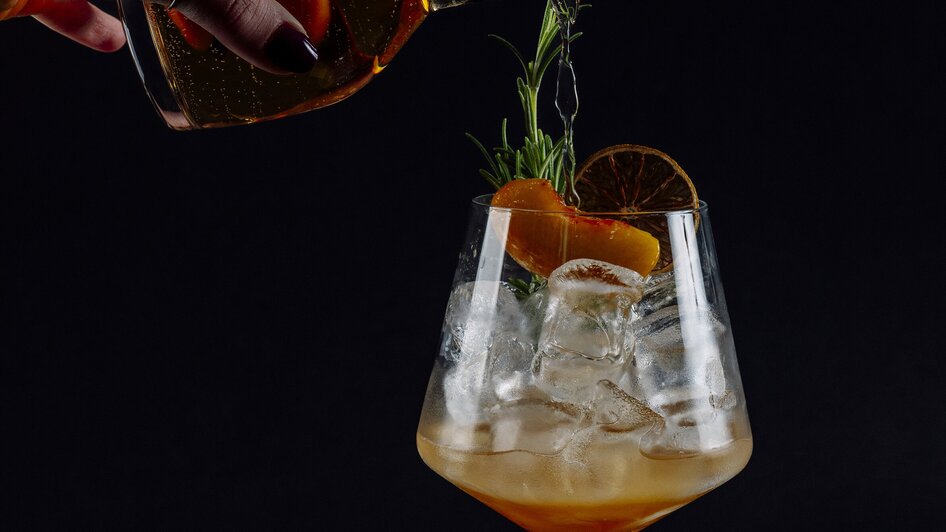 Ein Cocktail wird in ein großes Glas mit Eis gegossen.