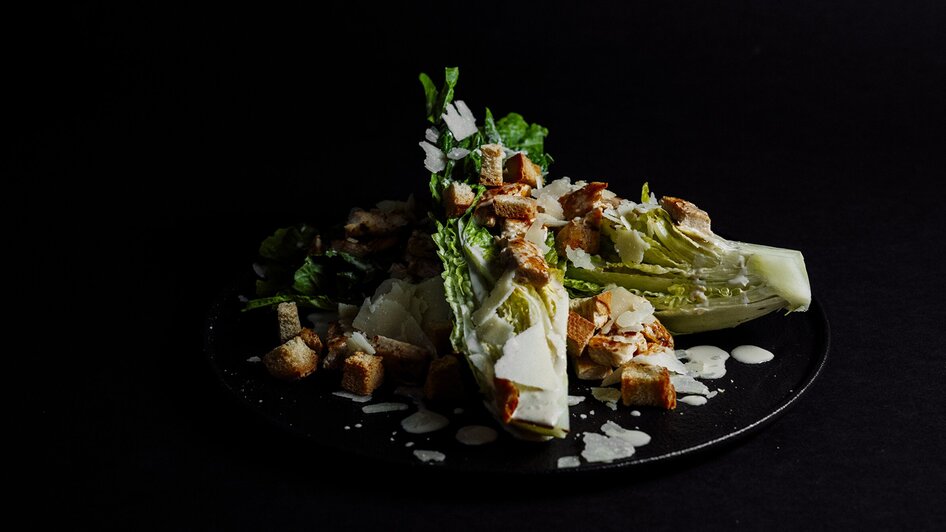 Frischer Cäsar-Salat mit Croutons und Parmesan auf schwarzem Hintergrund.