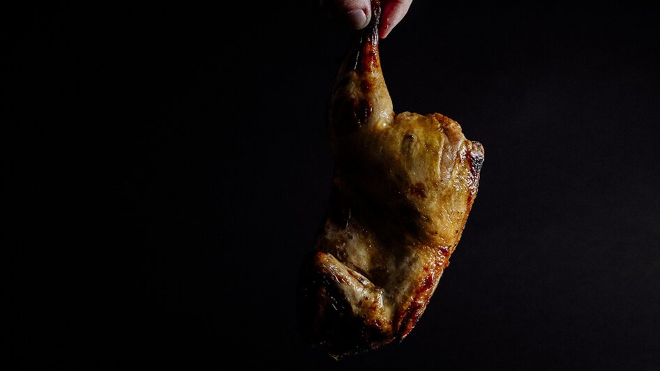 Gegrilltes Hähnchen wird über einer Platte mit Beilagen gehalten.