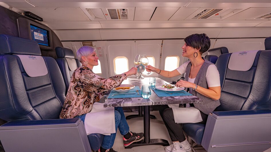 Zwei Frauen stoßen in einem Flugzeug im NOVA-AIR in Graz mit Gläsern an.