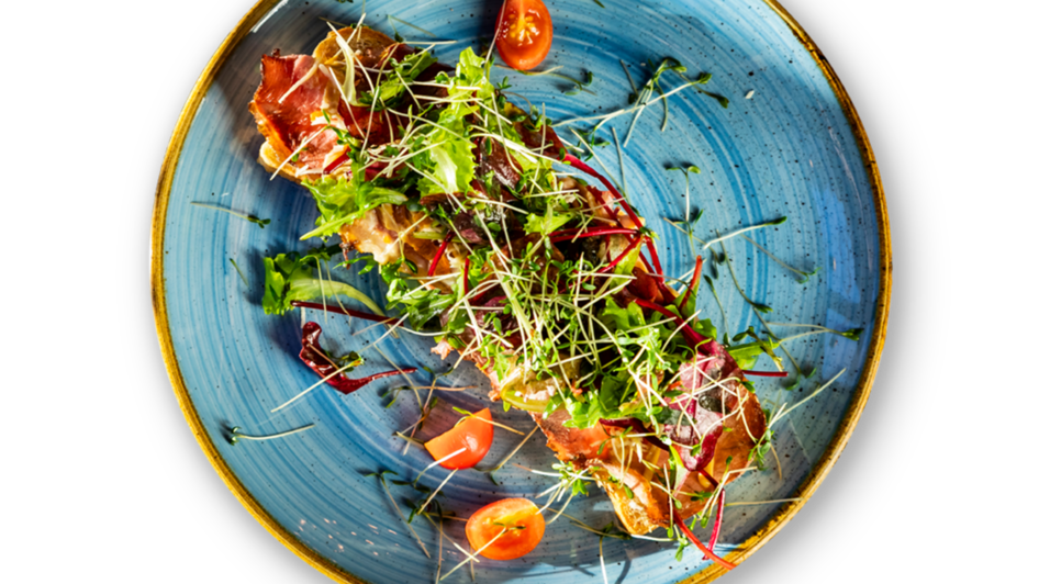 Ein elegantes Gericht mit Salat, Tomaten und frischen Kräutern auf einem blauen Teller.