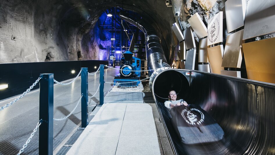 Ein Besucher auf der Schlossbergrutsche in Graz, in einem Tunnel mit Lichteffekten.