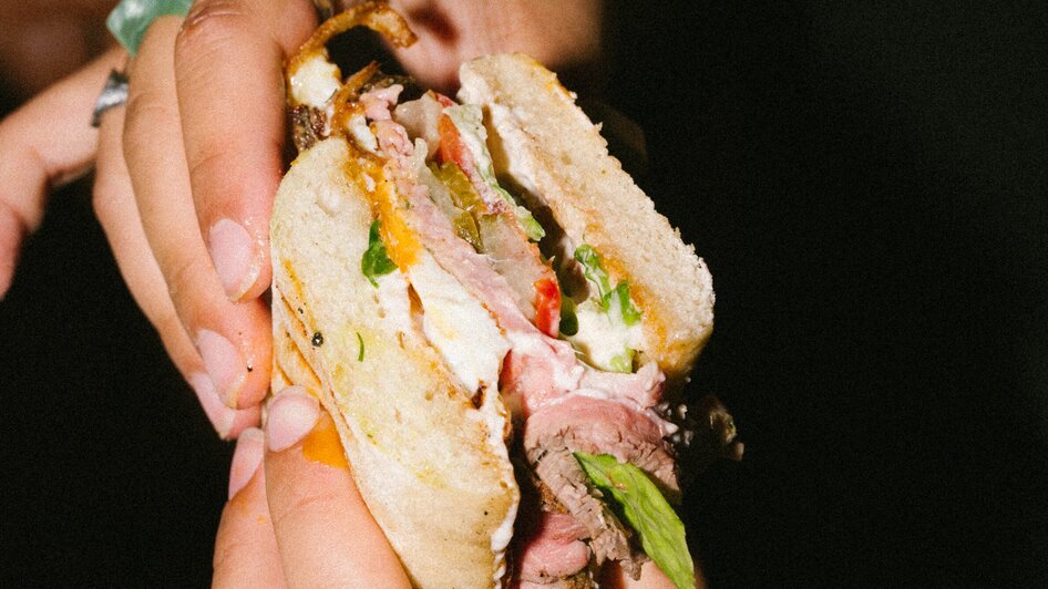 Eine Person hält ein Sandwich mit Rindfleisch und Salat.