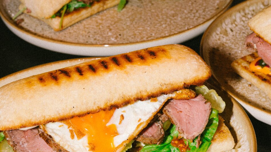 Ein gegrilltes Sandwich mit Rindfleisch, Spiegelei und frischem Gemüse.