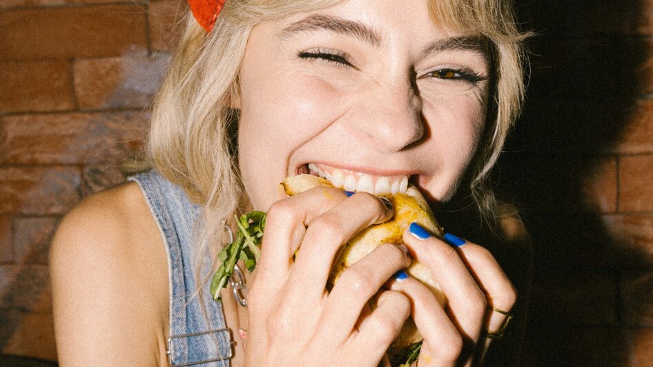 Eine Frau lächelt und genießt einen Burger, während sie breit grinst.