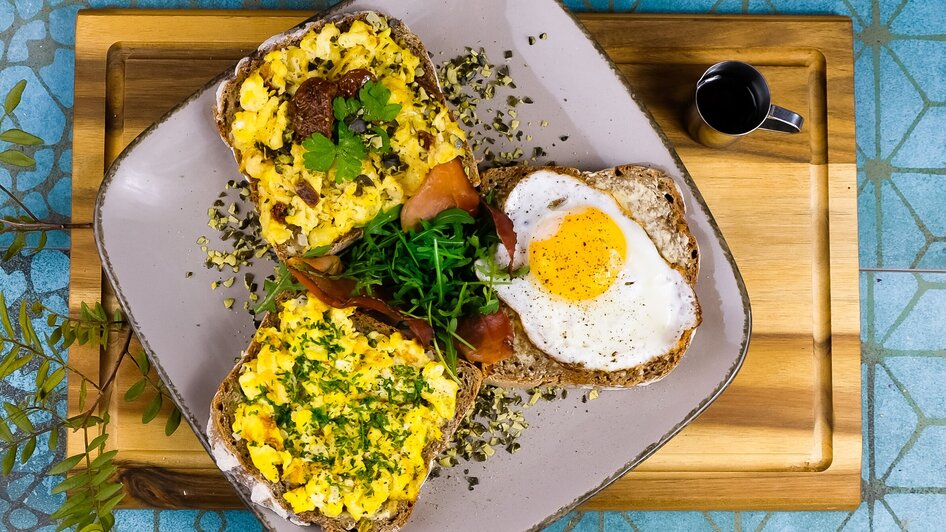 Frühstücksteller mit Rührei, Schinken und Salat auf Brot. | © Mona Ramsenthaler