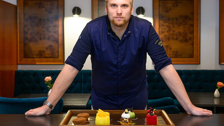 Küchenchef steht vor einem Tisch mit einer Platte mit verschiedenen Desserts in Graz. | © Zur Goldenen Birn