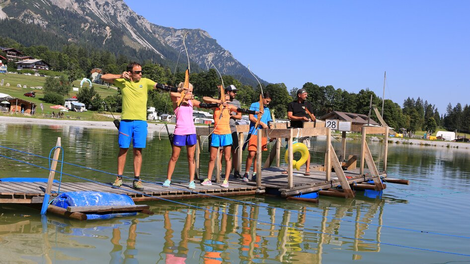 Gruppe am Bogenschießen steht auf einem Steg im Wasser. 