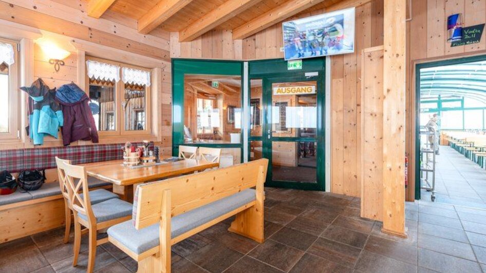 Gemütlicher Gastraum mit Holzwänden, Polsterbänken und Holztischen, warm beleuchtet.