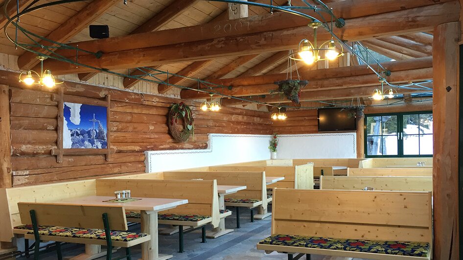 Wintergarten mit Holzwänden, Polsterbänken und Holztischen.